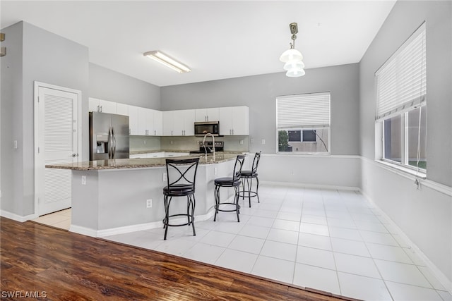 kitchen featuring light stone counters, white cabinets, a kitchen bar, light hardwood / wood-style floors, and stainless steel appliances