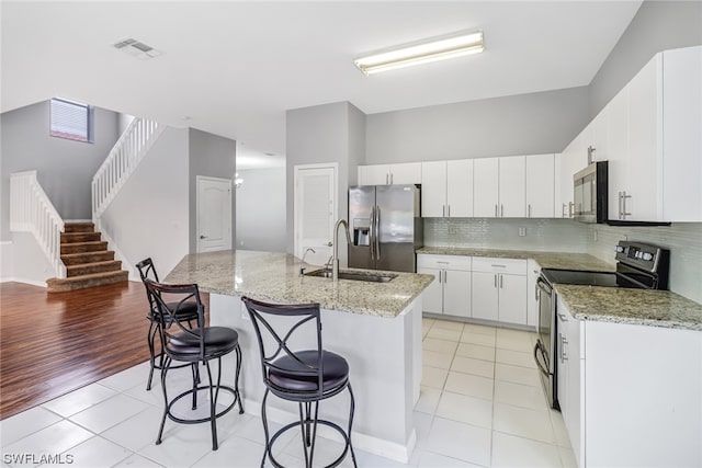 kitchen with appliances with stainless steel finishes, sink, light tile floors, and a kitchen island with sink