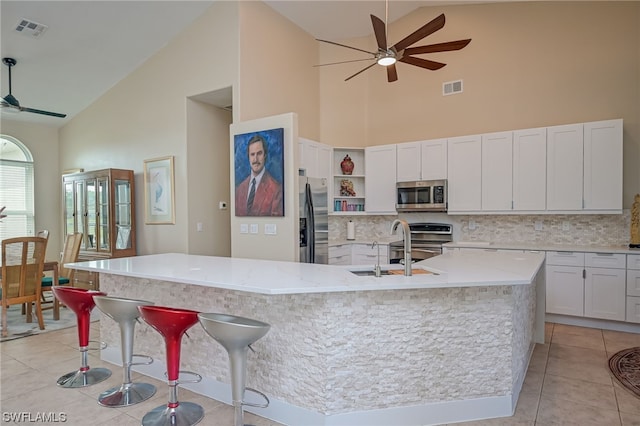 kitchen with a center island with sink, high vaulted ceiling, white cabinets, and appliances with stainless steel finishes