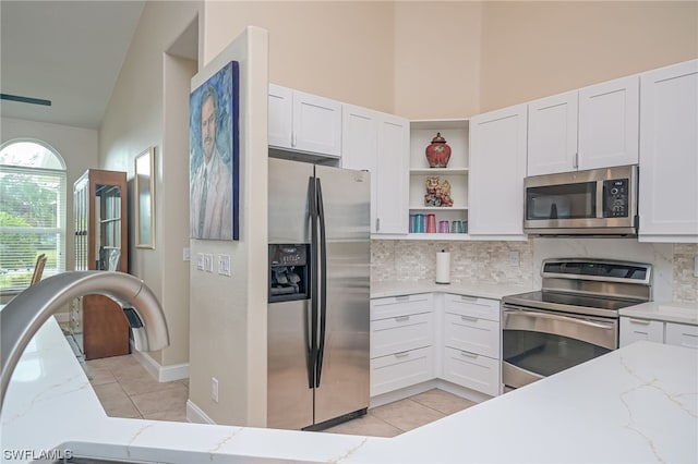 kitchen with light stone countertops, white cabinetry, stainless steel appliances, backsplash, and lofted ceiling