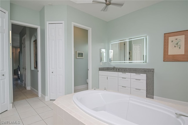 bathroom with vanity, tile patterned flooring, ceiling fan, toilet, and tiled bath