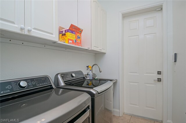 laundry area with washing machine and clothes dryer, light tile patterned flooring, and cabinets