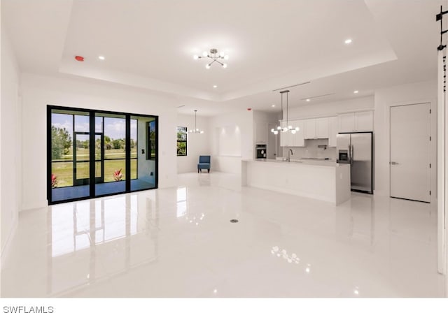 unfurnished room featuring a notable chandelier, sink, a tray ceiling, and light tile flooring