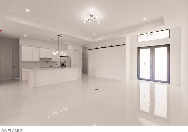 unfurnished living room with light tile floors, a notable chandelier, and a tray ceiling