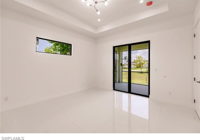 tiled spare room with a chandelier and a raised ceiling