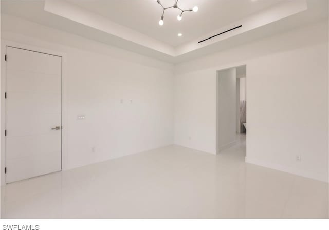 tiled empty room featuring a tray ceiling and a notable chandelier