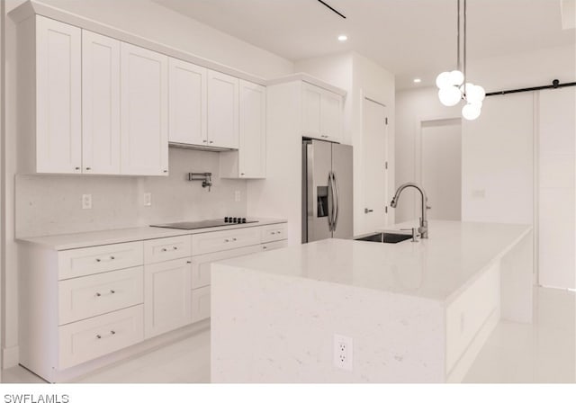 kitchen featuring stainless steel refrigerator with ice dispenser, white cabinetry, black electric stovetop, hanging light fixtures, and sink