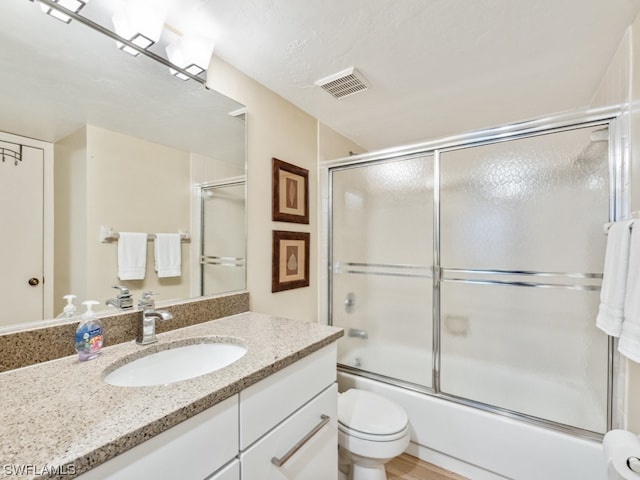 full bathroom with oversized vanity, toilet, a textured ceiling, and bath / shower combo with glass door