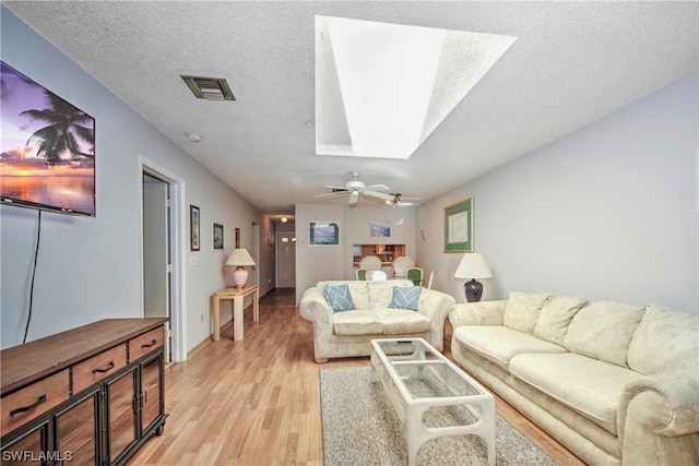 living room with a textured ceiling, a skylight, ceiling fan, and light hardwood / wood-style floors