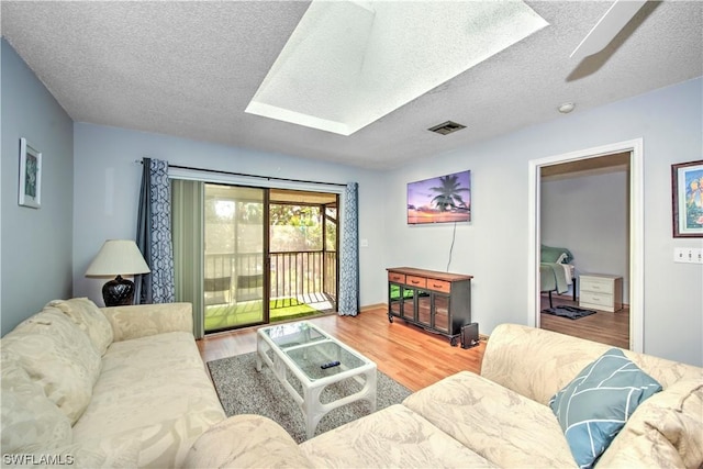 living room with a skylight, ceiling fan, light hardwood / wood-style floors, and a textured ceiling