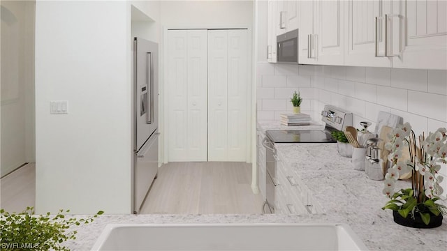 kitchen with light stone counters, light wood-type flooring, white cabinets, stainless steel appliances, and backsplash