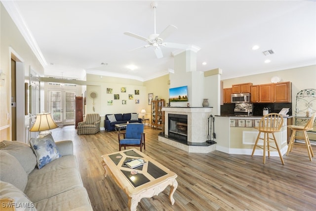 living room with french doors, ceiling fan, crown molding, a tile fireplace, and light hardwood / wood-style flooring