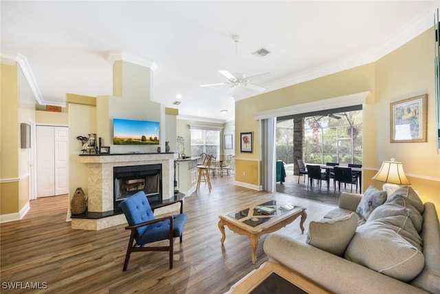 living room featuring dark hardwood / wood-style floors, ceiling fan, crown molding, and a tiled fireplace