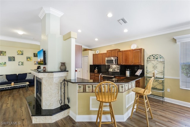 kitchen featuring hardwood / wood-style floors, crown molding, appliances with stainless steel finishes, kitchen peninsula, and a breakfast bar area