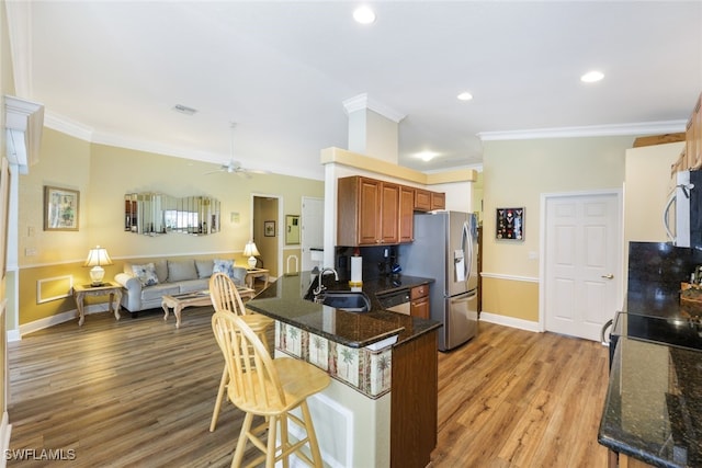 kitchen with ceiling fan, sink, crown molding, light hardwood / wood-style floors, and a breakfast bar area