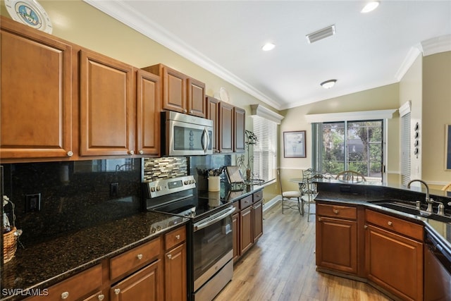 kitchen with appliances with stainless steel finishes, light wood-type flooring, ornamental molding, dark stone counters, and sink