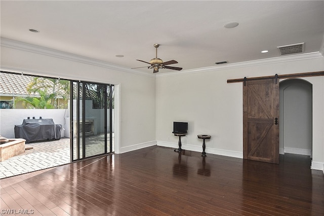 empty room featuring ceiling fan, a barn door, dark hardwood / wood-style flooring, and crown molding