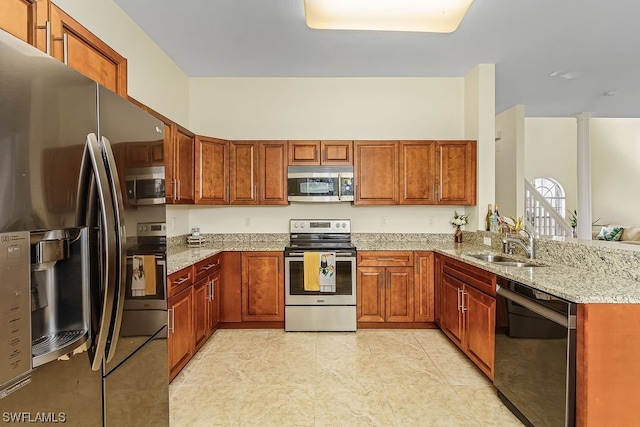 kitchen featuring light stone counters, stainless steel appliances, sink, and decorative columns