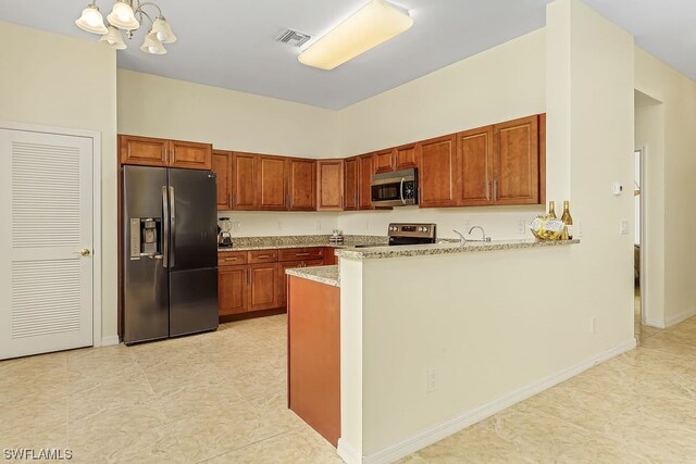 kitchen featuring kitchen peninsula, light stone counters, stainless steel appliances, a notable chandelier, and hanging light fixtures