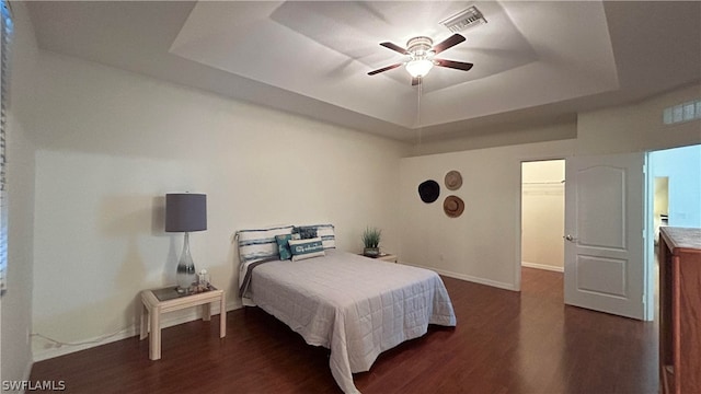 bedroom featuring ceiling fan, dark hardwood / wood-style flooring, a raised ceiling, and a walk in closet