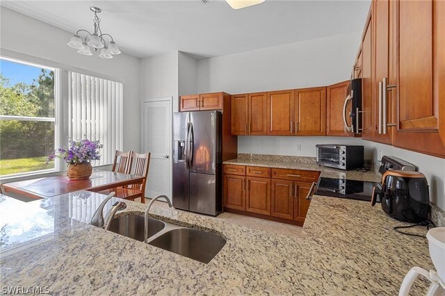 kitchen with appliances with stainless steel finishes, light stone counters, sink, pendant lighting, and an inviting chandelier