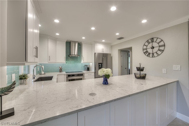 kitchen featuring light stone counters, backsplash, stainless steel appliances, wall chimney range hood, and white cabinetry