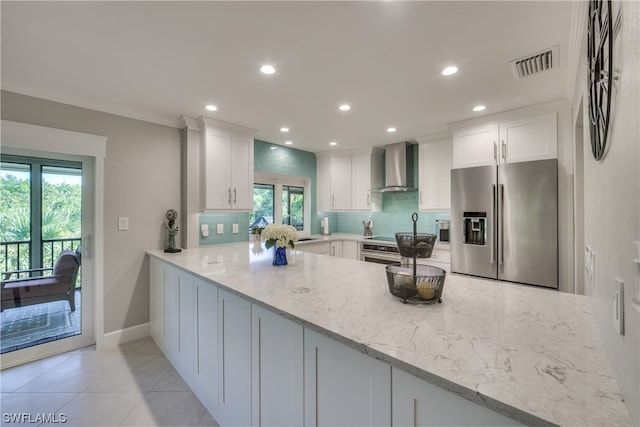 kitchen featuring white cabinets, stainless steel appliances, light stone counters, and wall chimney range hood