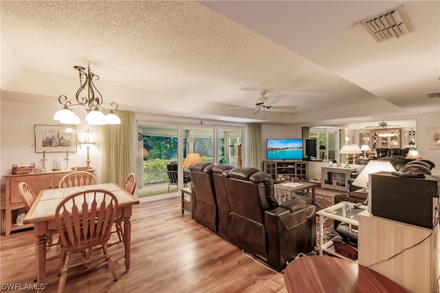 living room with a textured ceiling, ceiling fan with notable chandelier, a tray ceiling, and light hardwood / wood-style flooring