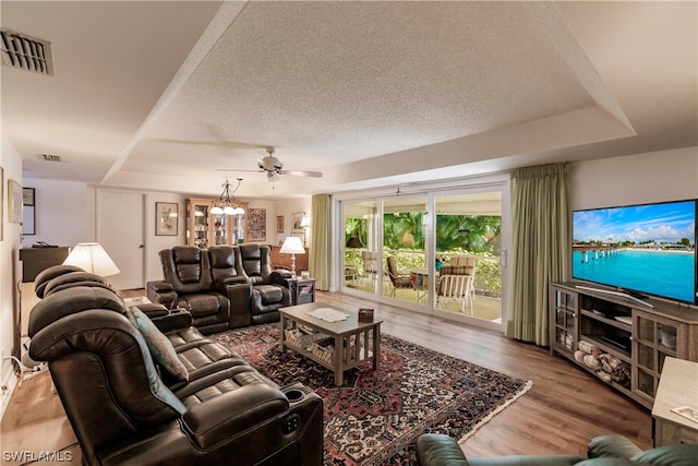 living room with a raised ceiling, a textured ceiling, wood-type flooring, and ceiling fan with notable chandelier