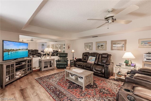 living room featuring dark hardwood / wood-style floors, a textured ceiling, ceiling fan, and a tray ceiling