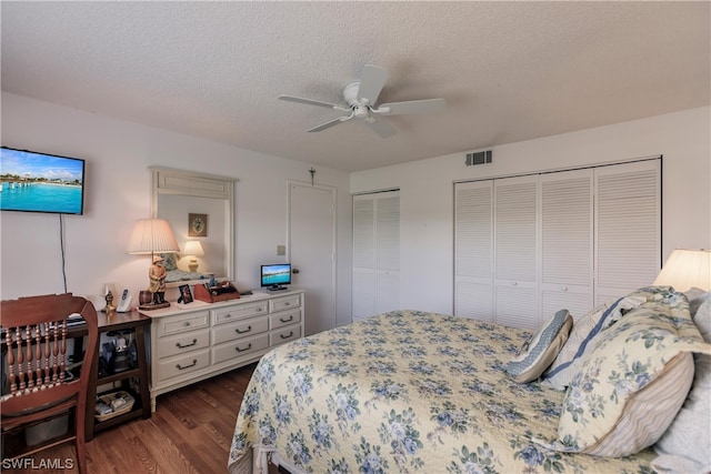 bedroom with two closets, dark hardwood / wood-style flooring, a textured ceiling, and ceiling fan