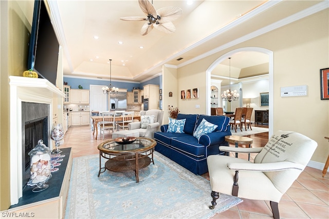 tiled living room with ceiling fan with notable chandelier, crown molding, a raised ceiling, and a fireplace