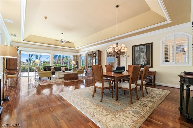 dining area featuring dark wood-type flooring, ceiling fan with notable chandelier, a tray ceiling, and ornamental molding