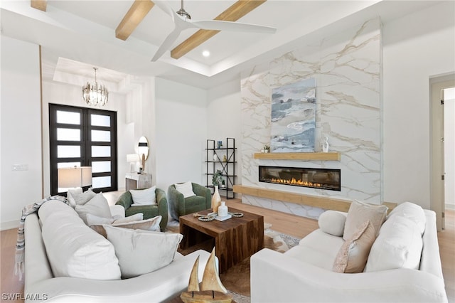 living room featuring ceiling fan with notable chandelier, a high end fireplace, wood-type flooring, and beamed ceiling