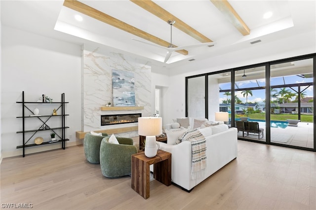 living room with wood-type flooring, beamed ceiling, a high end fireplace, a raised ceiling, and ceiling fan