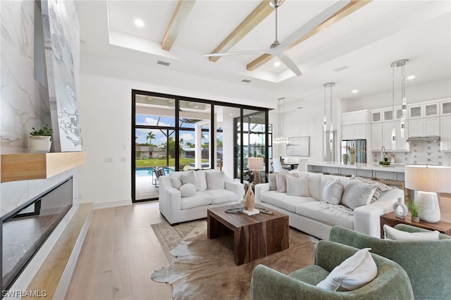 living room featuring beamed ceiling, ceiling fan, light wood-type flooring, and a fireplace