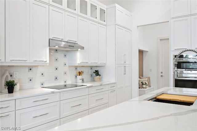 kitchen with double wall oven, black electric cooktop, white cabinets, and backsplash