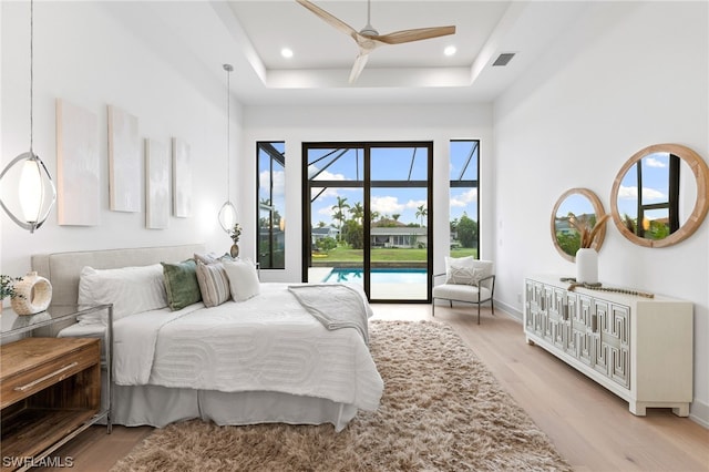 bedroom featuring a raised ceiling, ceiling fan, light wood-type flooring, and access to outside