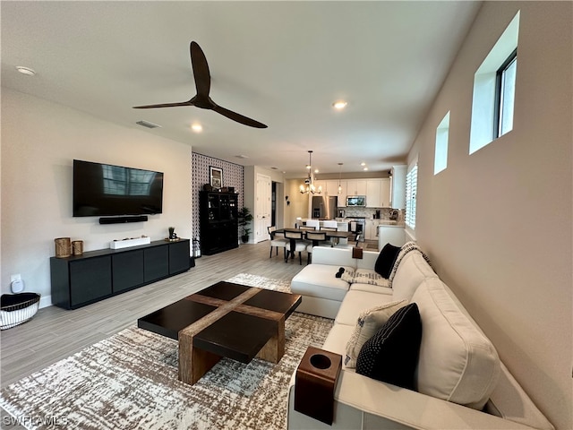 living room with ceiling fan with notable chandelier and light wood-type flooring