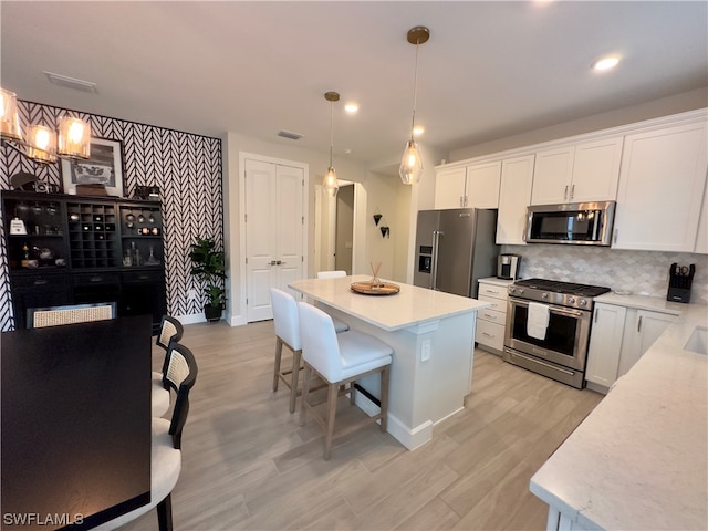 kitchen featuring decorative light fixtures, appliances with stainless steel finishes, a breakfast bar area, white cabinetry, and a center island