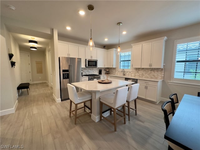 kitchen with a kitchen island, white cabinets, high quality appliances, backsplash, and decorative light fixtures