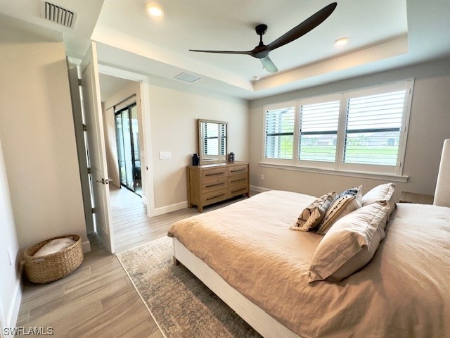 bedroom with ceiling fan, a raised ceiling, and light wood-type flooring