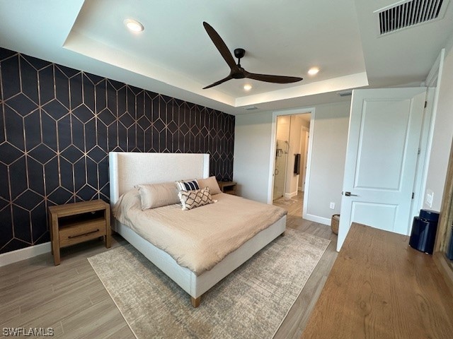 bedroom featuring hardwood / wood-style flooring, ceiling fan, and a tray ceiling