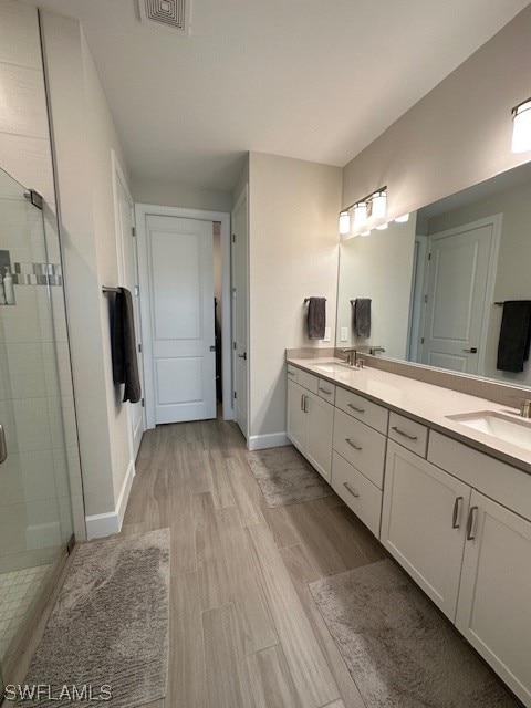 bathroom featuring a shower with door, wood-type flooring, oversized vanity, and double sink