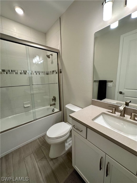 full bathroom with hardwood / wood-style flooring, vanity, toilet, and bath / shower combo with glass door