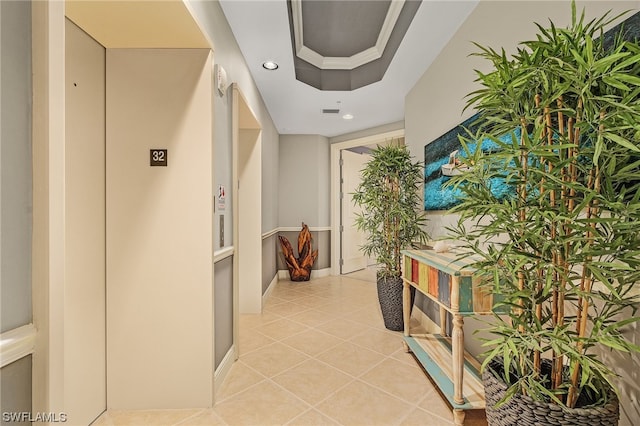 corridor featuring crown molding, a raised ceiling, and light tile flooring