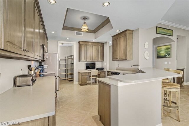 kitchen featuring kitchen peninsula, light tile flooring, a kitchen breakfast bar, sink, and a raised ceiling