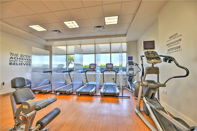 exercise room with light hardwood / wood-style floors and a paneled ceiling