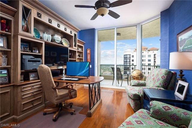 home office featuring expansive windows, wood-type flooring, and ceiling fan