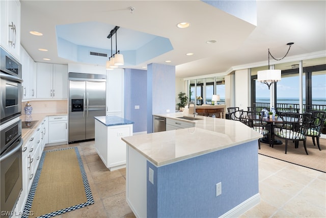 kitchen with appliances with stainless steel finishes, decorative light fixtures, sink, white cabinets, and a center island with sink